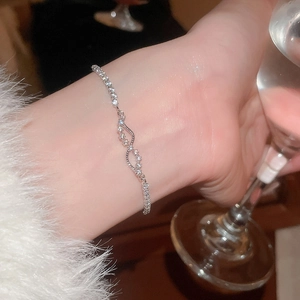 Macro shot of silver-toned zircon bracelet with infinity wave pattern on a female wrist