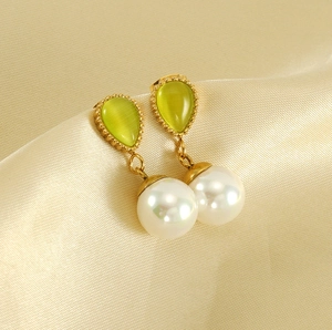 Detailed macro shot of gold teardrop earrings with green cat eye stone and white pearls