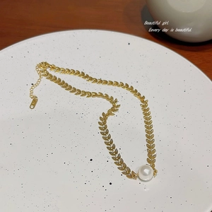 Detail of gold wheat leaf chain necklace featuring a single white pearl drop on a plate
