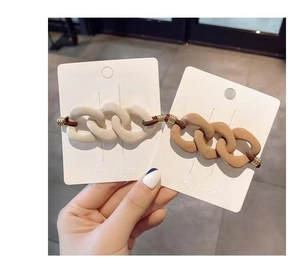 Detail of milk tea color chain-link hair ties set on card, held by a model's hand