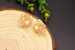 Detail of amber flower stud earring with white pearl on natural wood background