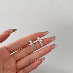 Detail shot of silver feather earrings with white zircon stones on a model's hand