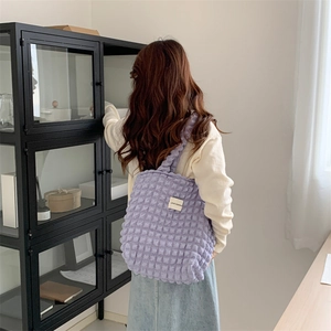Detailed view of purple bubble textured tote bag carried by model in a home setting