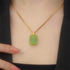 Elegant emerald green jade pendant necklace with gold chain worn on a black blazer