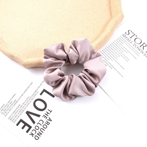 Detail of dusty rose satin silk scrunchie with soft sheen on a beige display tray