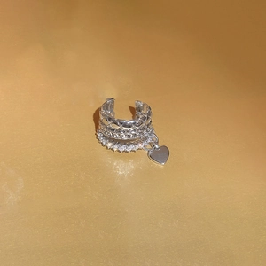 Detail of silver triple-layered ear cuff with zircon heart pendant on golden background