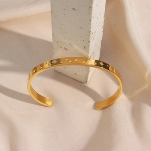 Macro shot of gold star engraved bangle with white zircon on elegant satin fabric
