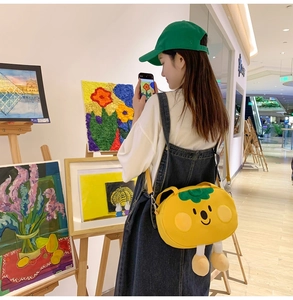 Detail of yellow cartoon persimmon crossbody bag with green leaves and plush legs