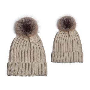 Matching parent-child beige knit beanies with large brown faux fur pom poms and ribbed texture