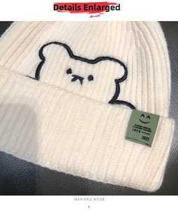 Detail of cream knit beanie featuring bear embroidery and smiley face fabric patch