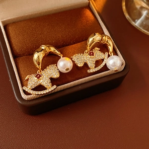 Macro shot of gold rocking horse earrings with pearls and crystals in a velvet box