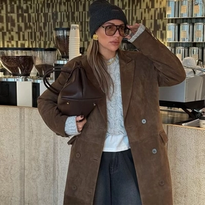 Détail d'un manteau long en daim marron porté avec un pull torsadé et un sac à main