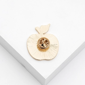 Macro view of the golden apple pin back showing radial texture and safety clasp