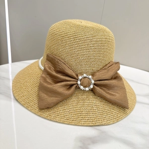 Elegant wide brim straw sun hat with pearl chain and brown bow on marble surface