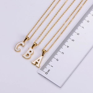 Detailed scale view of 18k gold alphabet pendants A, B, C with white shell inlay