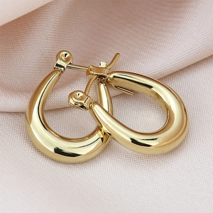 Close-up of polished gold U-shaped hoop earrings on elegant pink silk fabric background