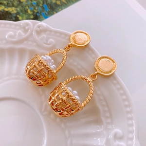 Close-up of golden basket-shaped earrings with white faux pearls on white ceramic