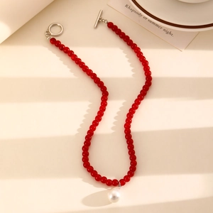 Detalle macro de collar de cuentas rojas con perla de gota blanca y cierre OT plateado