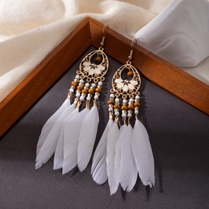 Detailed shot of bohemian long feather earrings with gold openwork and white beads