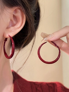 Detailed close-up of oversized burgundy glossy hoop earrings with a sleek minimalist design