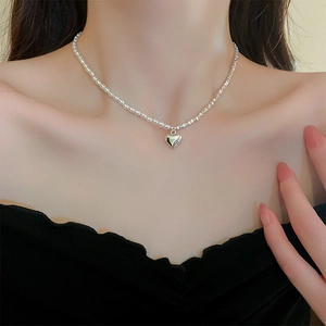 Detail of a layered necklace with white pearls and silver heart pendant on model