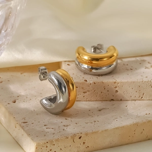 Detail von zweifarbigen gold-silbernen C-Ohrringen auf strukturiertem Stein und Seide