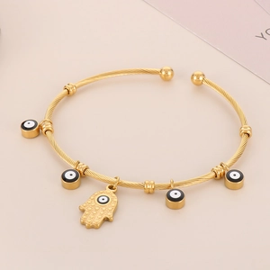 Detail of 18K gold stainless steel twisted bangle with Hamsa Hand and Evil Eye charms
