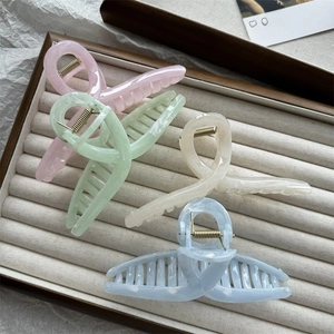 Detail showing four assorted marble-textured acetate hair claws on a beige velvet tray