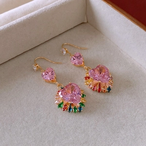 Close-up of golden hook earrings featuring pink heart stones and colorful gemstones