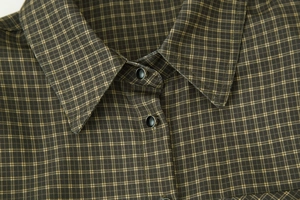 Detail shot of the sharp lapel collar and dark plaid fabric with metal-edged buttons