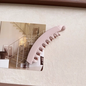 Close-up of pink matte banana hair clip on beige textured background with postcard