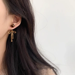 Close-up of elegant gold bow earrings with brown gemstone bead worn by a model
