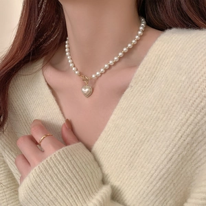 Elegant heart pearl necklace with diamond accents on white knit sweater