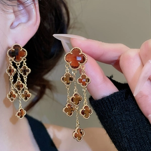 Macro shot of gold-plated clover leaf drop earrings with amber crystal tassels and beads