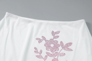 Close-up of white mesh fabric with pink rhinestone floral pattern and delicate texture