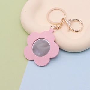 Pink flower-shaped PU leather mirror keychain on a cream tray with pastel background