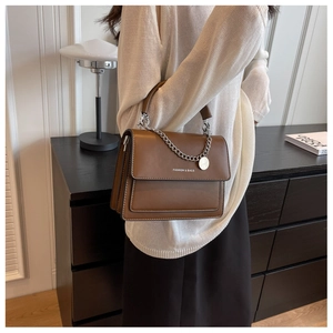 Detailed view of a brown leather shoulder bag with fashion text and silver chain strap