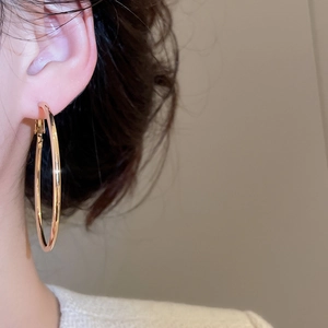 Close-up of a large polished gold circular hoop earring worn on a model's ear