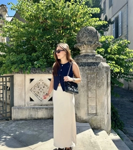 Photo en plein air d'un haut en maille sans manches avec jupe longue blanche et sac