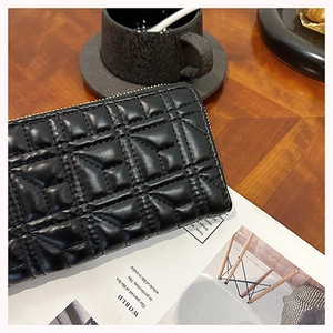 Detailed view of a black quilted leather zip wallet placed on a magazine with a coffee cup