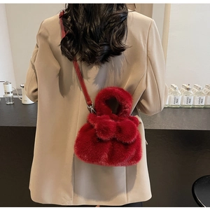 Detail of a red plush bucket bag with leather strap styled on a beige blazer model