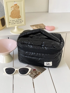Large black quilted makeup bag with handle and Soda Blue label on a white desk