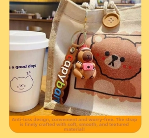Gros plan d'un porte-clés capybara avec mini caméra rose accroché à un sac en toile