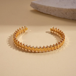 Detailed view of gold gear-textured geometric cuff bracelet on a stone pedestal