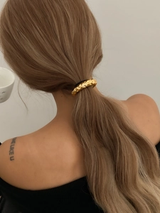 Macro shot of a textured golden ponytail cuff accessory on a minimalist hairstyle