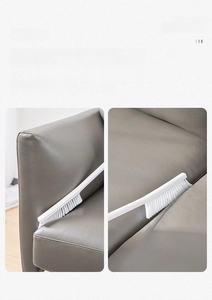 Macro view of long slim white brush head cleaning dust from grey leather sofa gaps