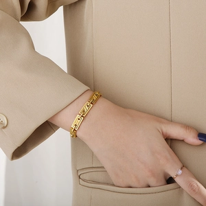 Close-up of golden geometric stainless steel bracelet worn on wrist with elegant ring