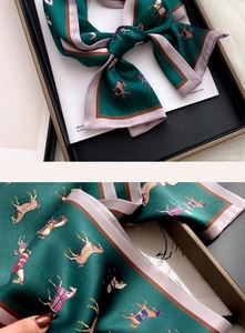 Detail of luxury silk scarf showing horse print on forest green satin fabric