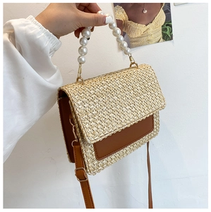 Detail of straw woven bag with pearl handle and brown leather base shown held by hand