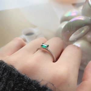 Close-up of emerald green zircon ring with sparkling diamond pavé band in soft light